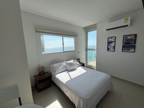 A bedroom with a bed, a nightstand, a window with a view of the sea, and a wall-mounted air conditioner. - OCEAN VIEW APARTMENT WIND 906 (Santa Marta)