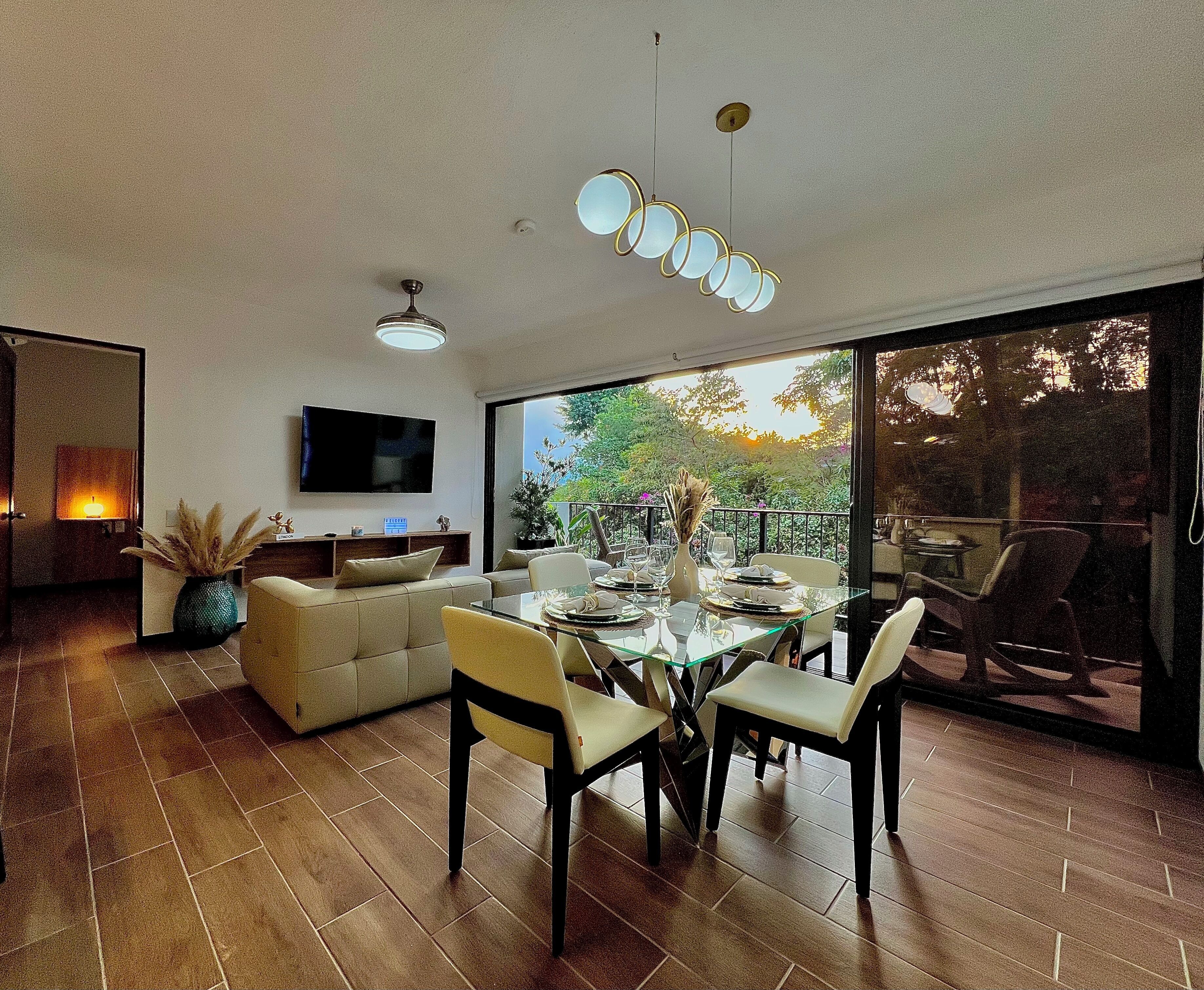 A modern dining area with a glass table, chairs, and a television mounted on the wall.