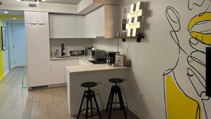 Een moderne keuken met witte kastjes, een koffieapparaat en een bar met krukken.