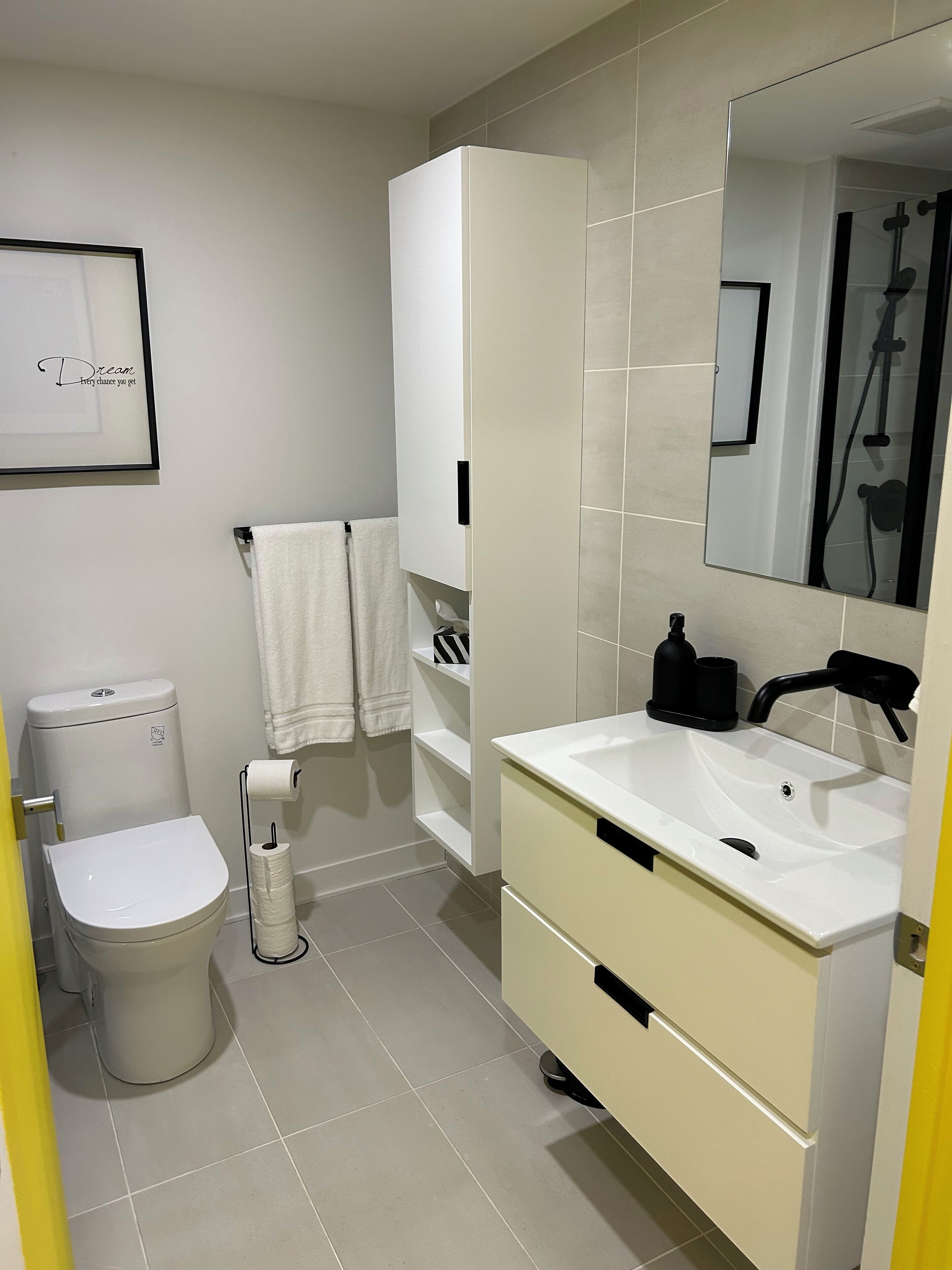 Un bagno moderno con servizi igienici, lavandino e specchio. Si nota un quadro appeso al muro e un portascopevoli con asciugamani.