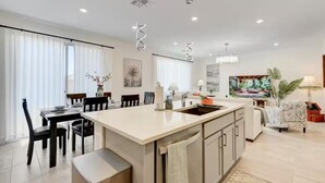 Une cuisine moderne dotée d’un îlot central, d’un coin repas avec des chaises et d’un espace de vie comprenant un canapé et un tableau.