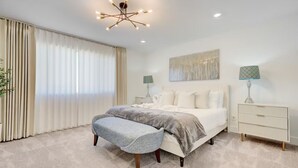Une chambre à coucher comprenant un lit, un banc, des tables de chevet et un luminaire fixé au plafond.