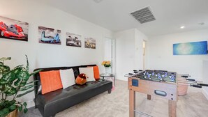 Un salon moderne avec un canapé, une table de baby-foot et des œuvres d’art murales.