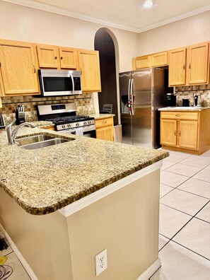 A kitchen with granite countertops, wooden cabinets, stainless steel appliances, and a tiled floor. - Spacious Retreat with Contemporary Comfort (Brandon)