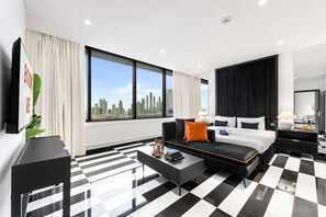 A modern hotel room with a large window, a black and white checkered floor, a black sofa, a bed, and a TV on the left wall. - Stayshort - 1 Bedroom in Difc That Sleeps 2 (Dubai)