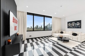 A modern living room with a black and white checkered floor, a white sofa, a black coffee table, and a large window with a city view. - Stayshort - 1 Bedroom in Difc That Sleeps 2 (Dubai)
