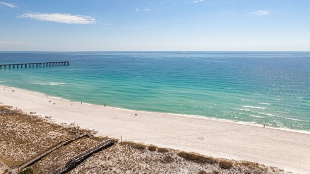 A beach with a wooden pier extending into the ocean, sandy beach, and clear blue sky. - Lemon Drop Beach Cottage (Navarre)