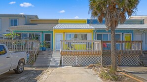 A row of beach houses with a wooden deck and a palm tree. - Lemon Drop Beach Cottage (Navarre)