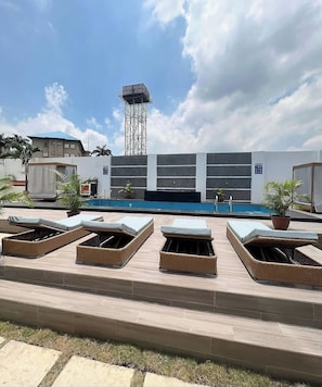 A rooftop pool area with lounge chairs, a pool, and a building in the background. - BUGE HOMES (Abuja)