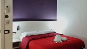 A bedroom with a red bedspread, white pillows, a bedside table, and a wall-mounted control panel. - Casa Maluma - Double Room with Kitchenette in the Heart of Naples (Napoli)