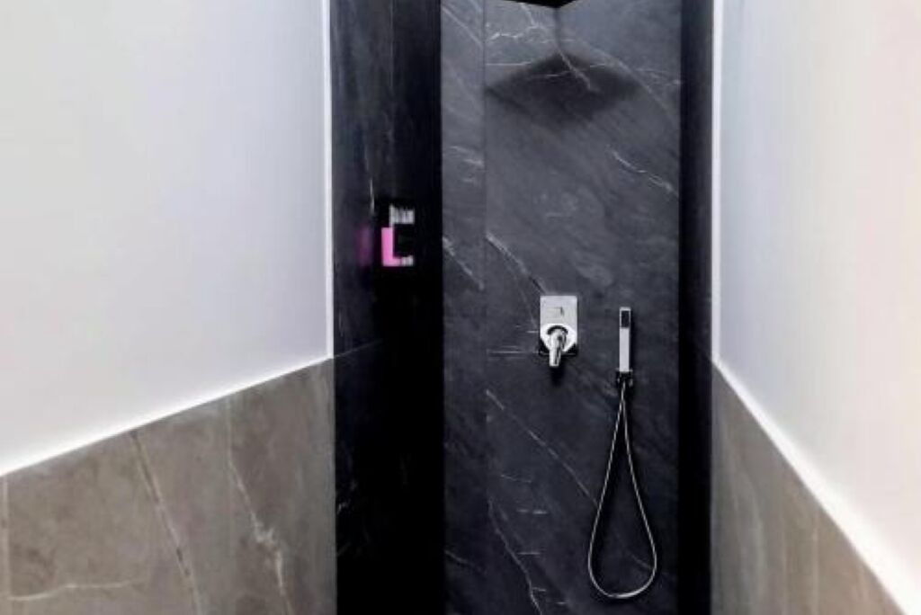 Un bagno moderno con box doccia in marmo nero, pannello comandi a vista e doccetta manuale.