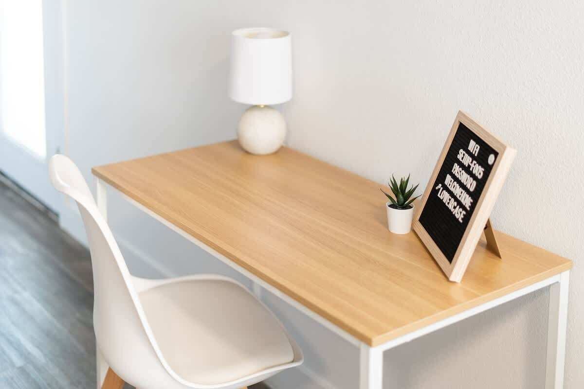 A small wooden desk with a white chair, a white lamp, and a small potted plant.