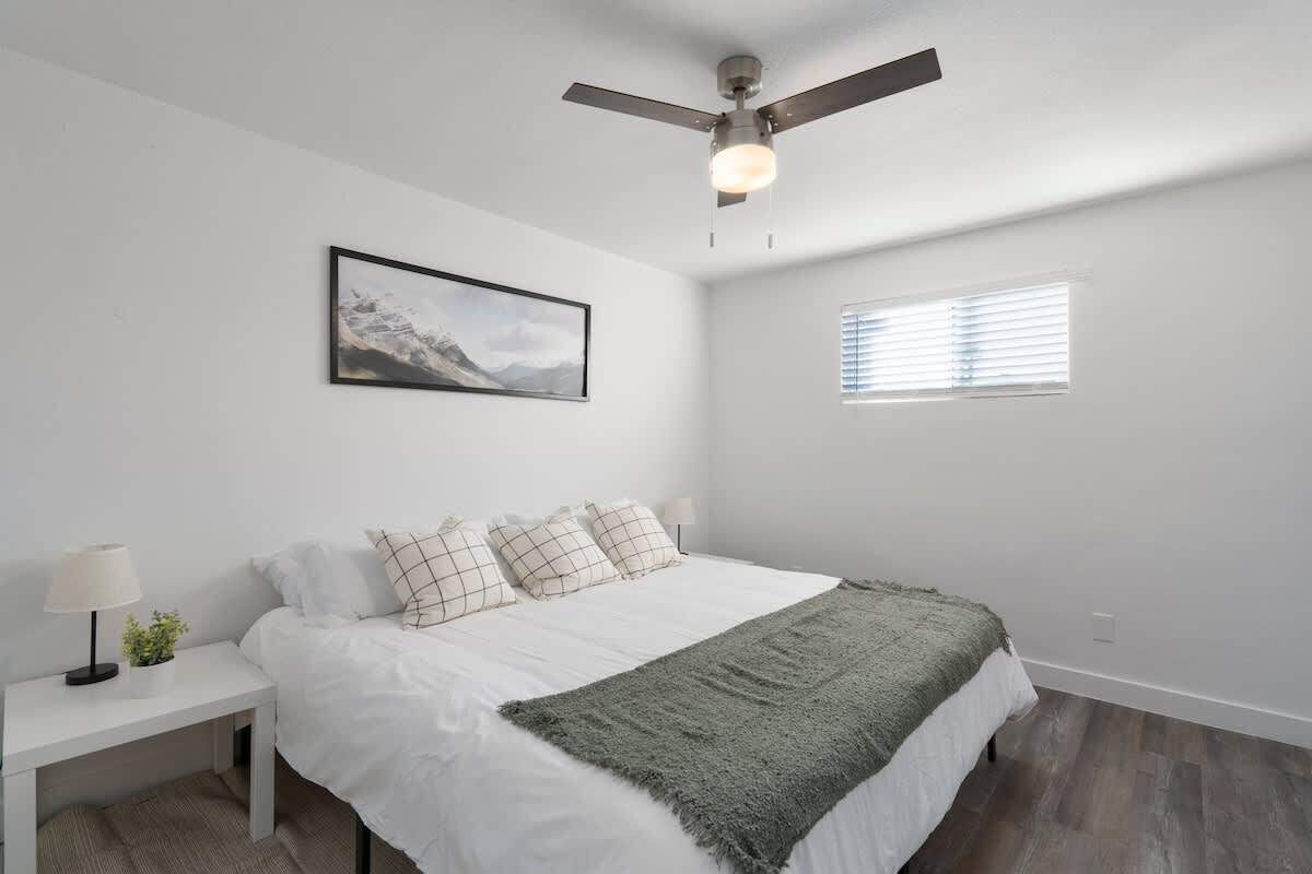 Une chambre à coucher avec un lit, un ventilateur de plafond, une fenêtre et un tableau accroché au mur.