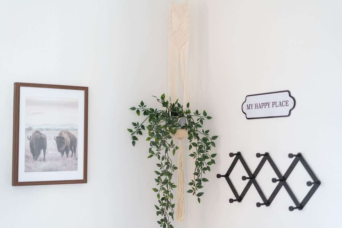 En væg med et indrammet billede af bisonokser, en hængende plante, et macramé-ophæng og et skilt med teksten "MY HAPPY PLACE".