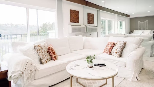 A spacious living room with a white sectional sofa, a marble coffee table, and large windows offering a view of the outdoors. - Hotel California" La Costa Resort Life (Carlsbad)