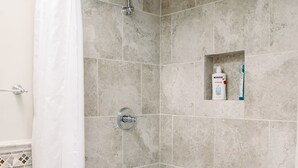 A bathroom with a bathtub, shower, and a small shelf with toiletries. - Hotel California" La Costa Resort Life (Carlsbad)