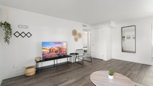 Ett modernt vardagsrum med en platt-TV, ett runt bord med en växt och en bänk med dekorativa föremål.