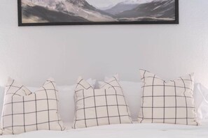 Un lit avec une literie blanche et trois oreillers à motifs géométriques.
