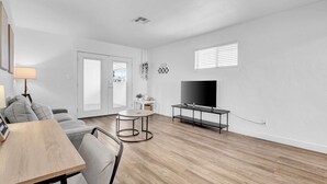 A modern living room with a wooden floor, a sofa, a round table, a TV on a stand, and a door leading to a balcony. - King, Parking | Steps from Phoenix Art Museum (Phoenix)