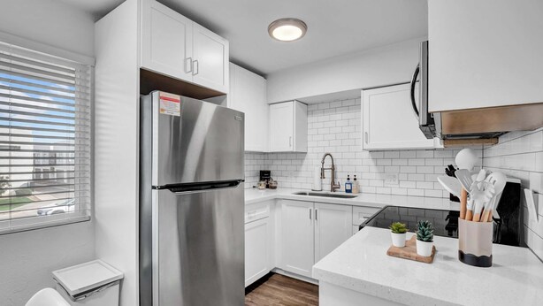 A modern kitchen with white cabinets, a stainless steel refrigerator, a built-in oven, and a countertop with a sink and various kitchen utensils. - King, Parking | Steps from Phoenix Art Museum (Phoenix)