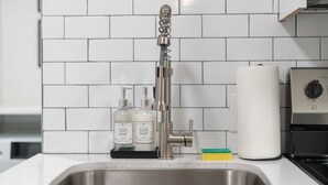 Un évier de cuisine doté d’un robinet moderne, deux bouteilles de liquide vaisselle, un porte-serviettes en papier et un distributeur de liquide vaisselle.