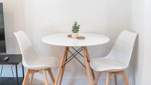 Une petite table ronde blanche, accompagnée de deux chaises blanches, d’une petite plante en pot et de quelques dessous de verre.