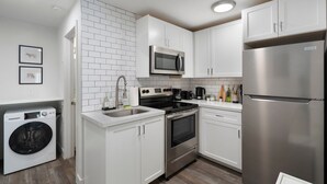 Une cuisine moderne avec des meubles blancs, des appareils en acier inoxydable et un lave-linge encastré.