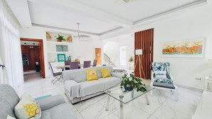 Ein modernes Wohnzimmer mit einer Couch, Sesseln, einem Glastisch und einem Essbereich mit Stühlen und einem Tisch.