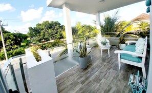 Een balkon met witte meubels, potplanten en uitzicht op groen en gebouwen.