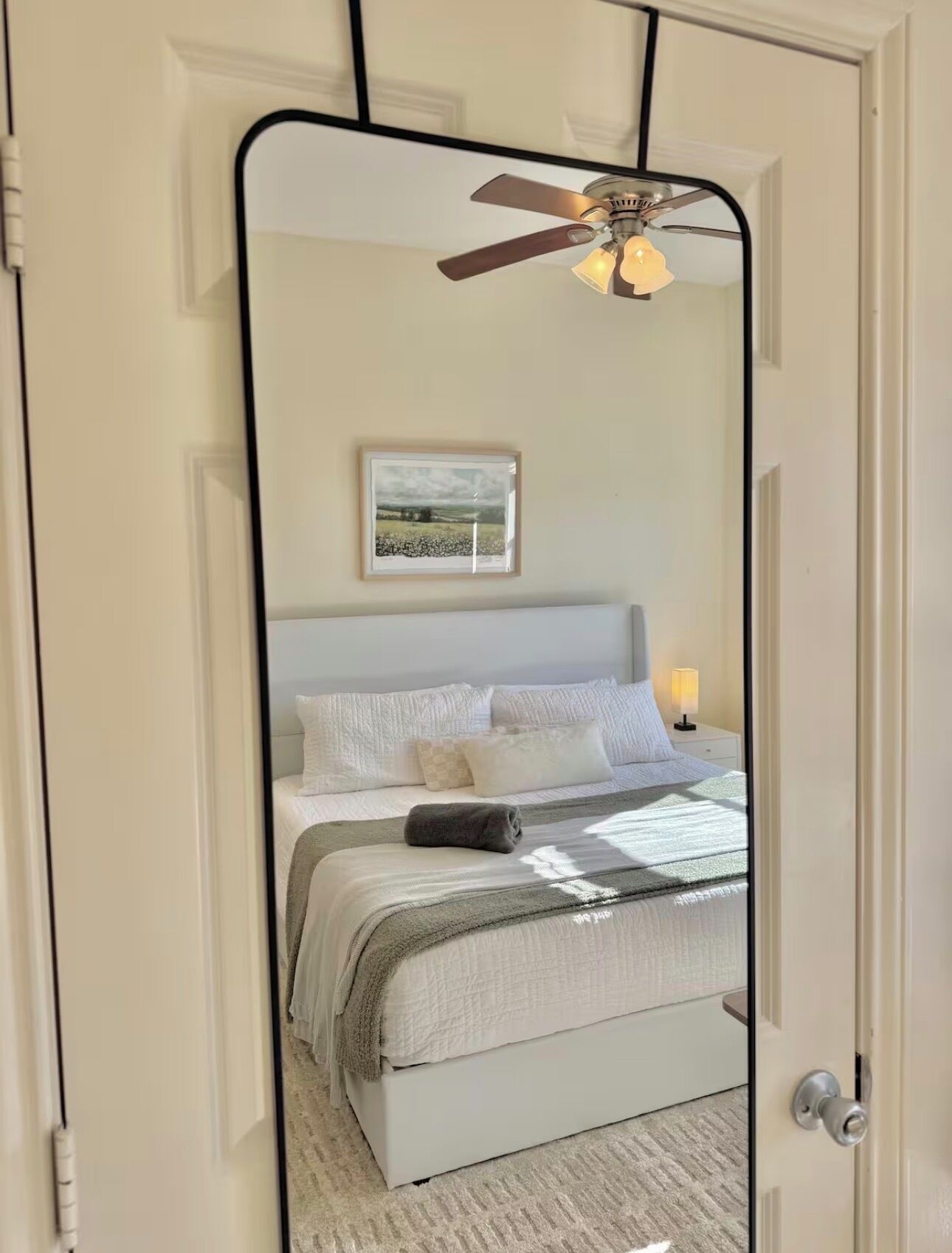 A bedroom with a bed, a nightstand, a lamp, a ceiling fan, and a framed picture on the wall.