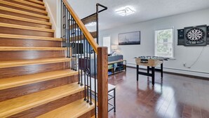 A wooden staircase with a black railing leading to a living area with a foosball table, a dartboard, and a painting on the wall. - Remodeled 4BR w/ Yard, Fire Pit, Near Camelback (Tannersville)