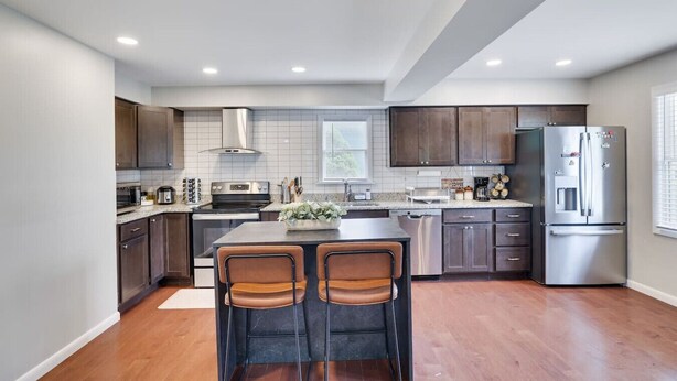 A modern kitchen with dark wood cabinets, a stainless steel refrigerator, and a central island with two chairs. - Remodeled 4BR w/ Yard, Fire Pit, Near Camelback (Tannersville)