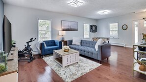 A living room with a blue sofa, a white coffee table, and a grey sofa. There is a television, a lamp, and a window with blinds. - Remodeled 4BR w/ Yard, Fire Pit, Near Camelback (Tannersville)