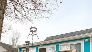 Una scala in legno conduce a un edificio con un cartello 'WELCOME', una finestra con cornice decorativa e un lampione in metallo.