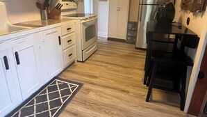 Cucina con mobili bianchi, un forno a microonde, un forno, un frigorifero e una sedia nera.