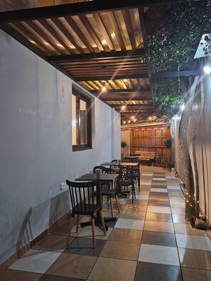 An outdoor patio with wooden tables and chairs, a checkered floor, and a wooden ceiling. - Haku Hostel Lima (Lima)