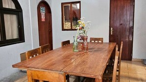 A wooden dining table with six chairs, a vase with flowers, and a sign on the door. - Haku Hostel Lima (Lima)