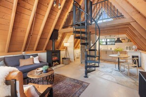 A spacious loft with a high ceiling, a built-in staircase, a cozy living area with a sofa, a coffee table, and a fireplace. - A-Frame Cabin & Romantic Retreat (Pine)