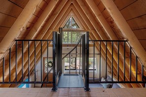 An attic room with a wooden ceiling, a metal staircase, and a view of the outdoors. - A-Frame Cabin & Romantic Retreat (Pine)