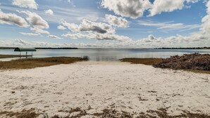 A sandy beach with a bench and a small structure, overlooking a calm body of water under a partly cloudy sky. - Water Access + Beach Area: Crooked Lake Escape (Babson Park)