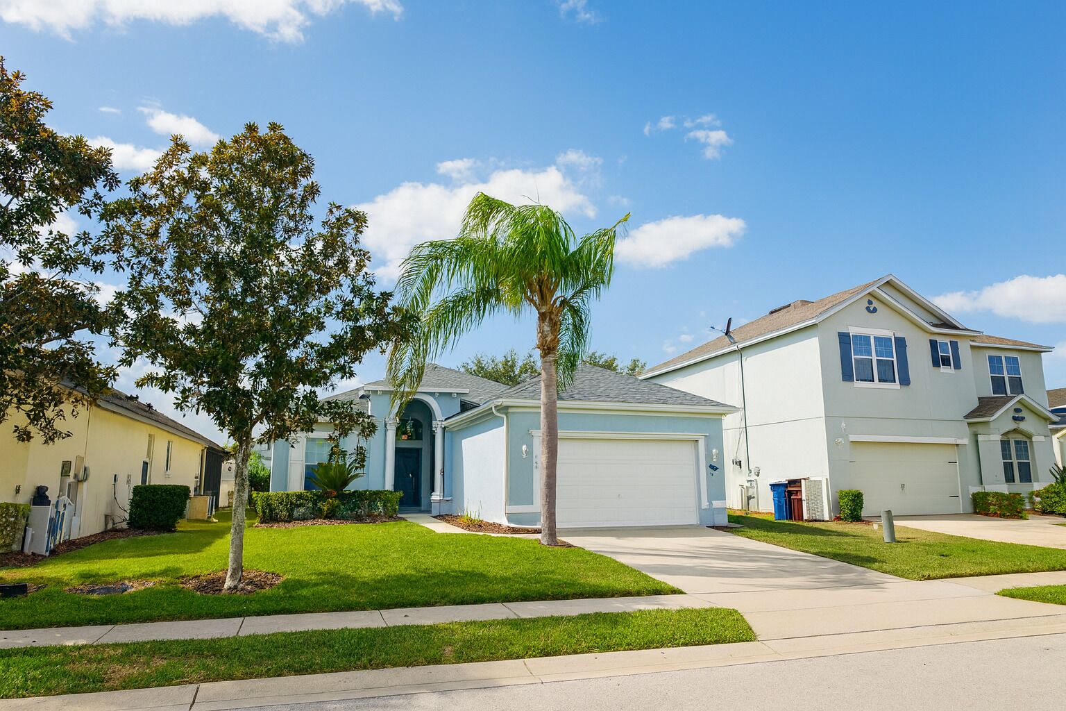 A suburban neighborhood with single-family homes, well-maintained lawns, and a clear blue sky.