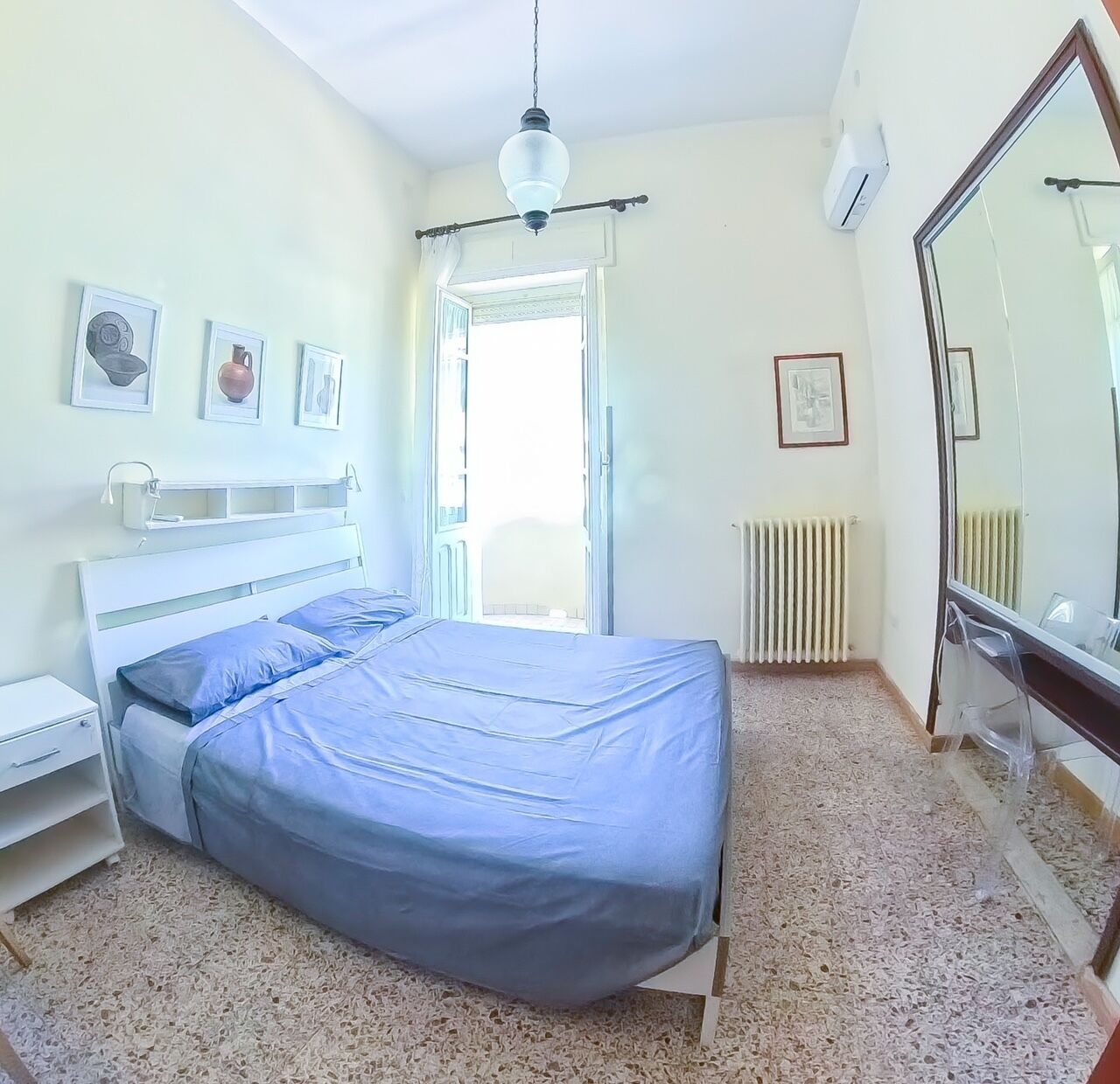 Una camera da letto con un letto, un comodino, uno specchio e un termosifone.
