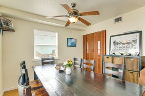 Un coin repas comprenant une table en bois, des chaises, un ventilateur de plafond et une fenêtre avec des stores.