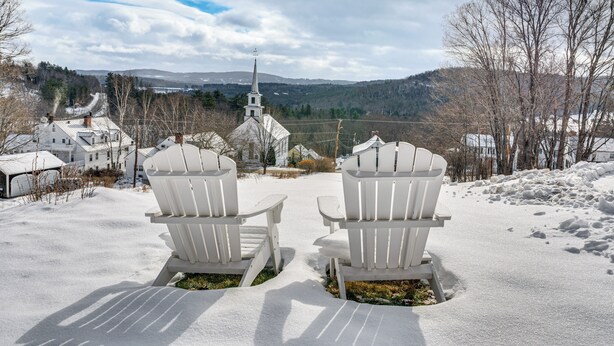 Two white Adirondack chairs facing a snow-covered landscape with a church and hills in the background. - Dine & Unwind! Overlook Home at Rabbit Hill Inn (Lower Waterford)