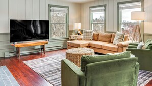 A living room with a sectional sofa, a television, a lamp, and a large window with blinds. - Dine & Unwind! Overlook Home at Rabbit Hill Inn (Lower Waterford)