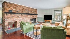A living room with a brick fireplace, green sofas, a television, and a lamp. - Dine & Unwind! Overlook Home at Rabbit Hill Inn (Lower Waterford)