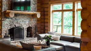 L’intérieur chaleureux d’un chalet en bois comprend une cheminée en pierre, un grand téléviseur à écran plat et un coin salon confortable avec un canapé et une table basse.