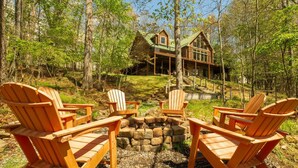 Une cabane avec un foyer en pierre, entourée de fauteuils Adirondack.
