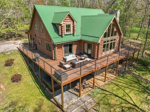 A log cabin with a green roof, a deck, and a covered outdoor seating area.