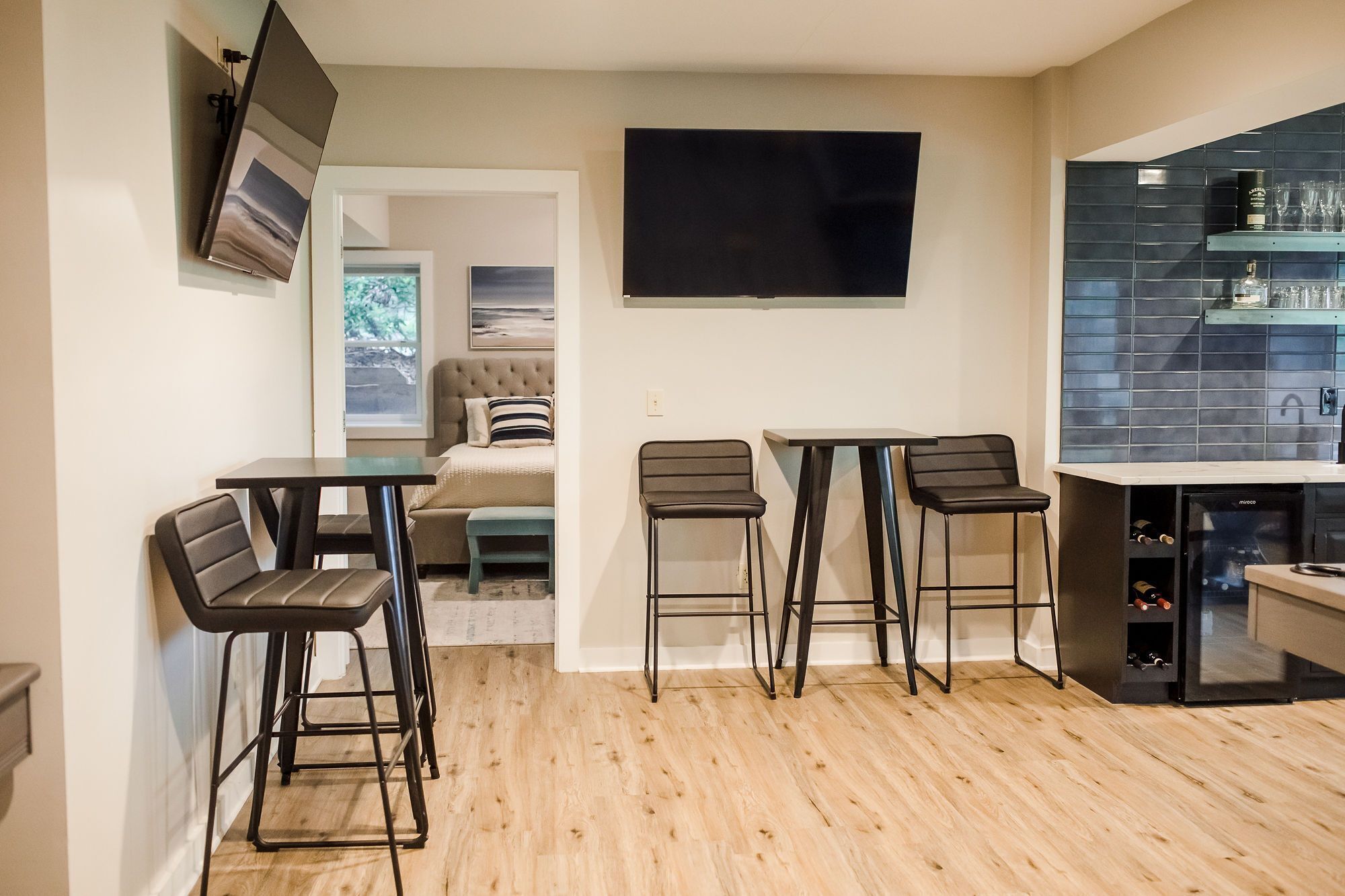 A modern kitchen with a dining area, a TV mounted on the wall, and a wine refrigerator.